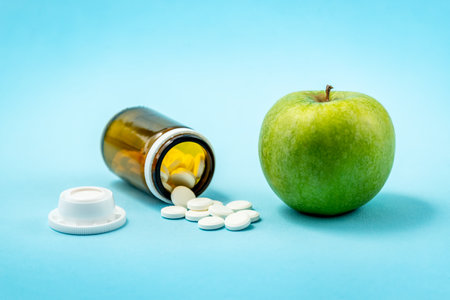 Green apple versus bottle of spilled pills - medicaments isolated on blue background. Concepto of medicaments and healthの写真素材