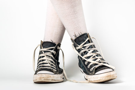 Old blue sneakers hipster style on girl legs in over the knee socks, on a white backgroundの写真素材