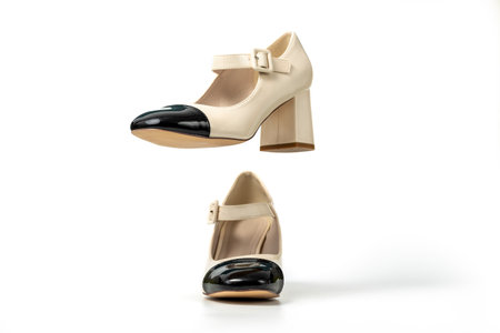Studio photo of a Retro style pair of high heel women's shoes on a white background. Patent leather buckle female shoes. Beige high heel shoes with black tipの写真素材