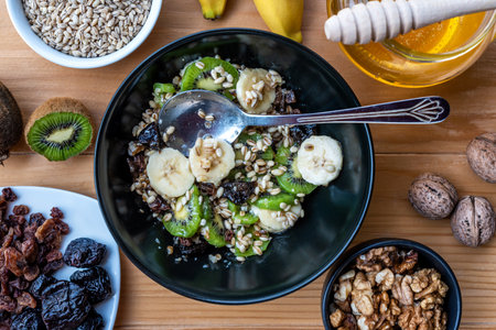 Healthy breakfast. Soaked organic raw barley, walnuts, kiwi, banana, raisins, prunes and honey on the table, wooden backgroundの写真素材