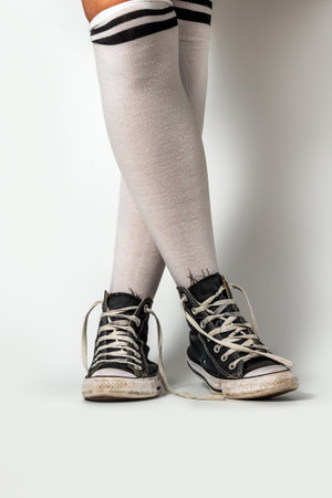 Old blue sneakers hipster style on girl legs in over the knee socks, on a white backgroundの写真素材