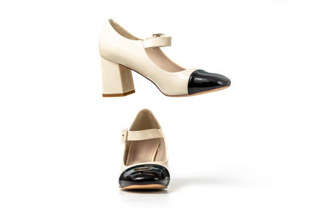 Studio photo of a Retro style pair of high heel women's shoes on a white background. Patent leather buckle female shoes. Beige high heel shoes with black tipの写真素材