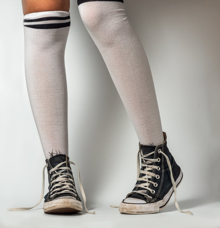 Old blue sneakers hipster style on girl legs in over the knee socks, on a white backgroundの写真素材