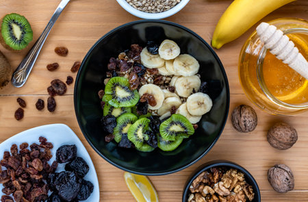 Healthy breakfast. Soaked organic raw barley, walnuts, kiwi, banana, raisins, prunes and honey on the table, wooden backgroundの写真素材