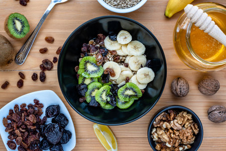 Healthy breakfast. Soaked organic raw barley, walnuts, kiwi, banana, raisins, prunes and honey on the table, wooden backgroundの写真素材