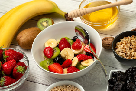 Healthy breakfast. Soaked organic raw barley, strawberries, walnuts, kiwi, banana, raisins, prunes and honey on the table, wooden backgroundの写真素材