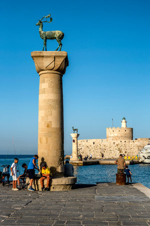 Rhodes, Greece. July 3, 2024: Harbor Gates and Lighthouse in Rhodes with fishermen and touristsのeditorial素材