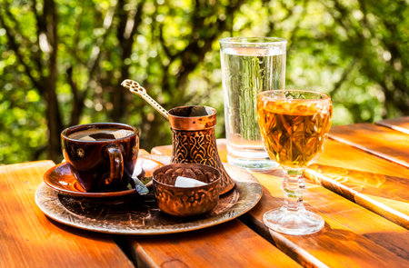 Black coffee in a cup, vintage copper coffee pot and a glass of domestic brandy on a rustic wooden tableの写真素材