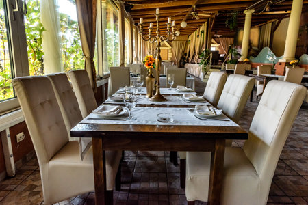 Interior modern restaurant, setting, serving banquet, degustation, table cloths, serving table, wine glasses, plates, cutlery near large window. Concept table set ready for diningの写真素材