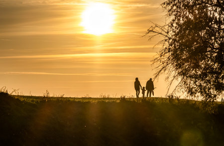 Happy family of three silhouettes walking at sunset. Parents and their child enjoying walk in natureの写真素材