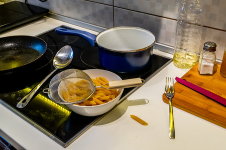 Cooking raw pasta in a pot on a cooker on a kitchen