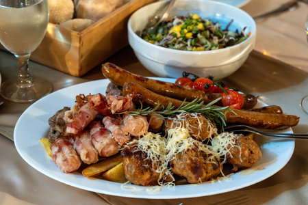 Plate on a restaurant table with sausages, meatballs, steak skewers, bacon, cherry tomatoes and...