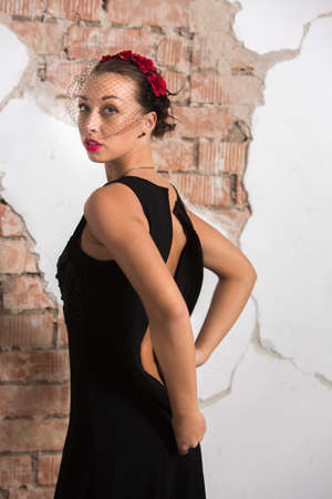 Sexy young girl in a long black dress with heels, with red lips and an attractive smile floral rim in her hair poses in the loft studio intimately taking off the dressの写真素材