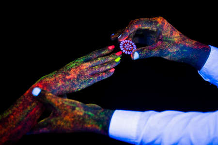 concept of connecting hands creative wedding photography in neon light male and female palms together hold on to each other the guy makes an offer with an engagement ring and the paint on them glow in the dark under the ultravioletの写真素材