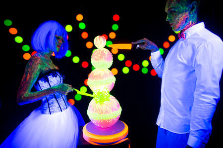 Neon photography bright colorful on a dark background in the rays of ultraviolet steam in love guy and girl bride with groom at a wedding cut wedding cake UV radiationの写真素材