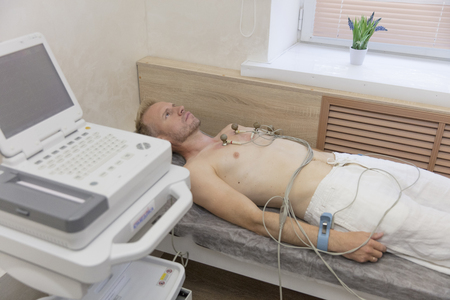 doctor with electrocardiogram equipment making cardiogram test to male patient in hospital clinicの写真素材