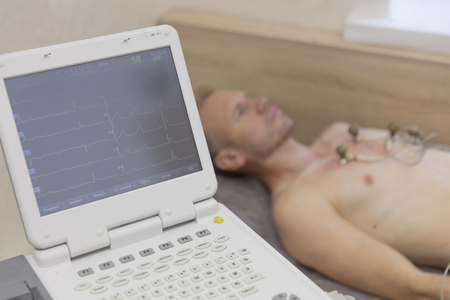 life monitoring doctor with electrocardiogram equipment making cardiogram test to male patient in hospital clinicの写真素材