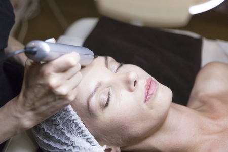 closeup portrait of happy young woman and hand with cosmetic lifting device touching her face