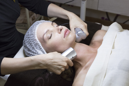 closeup portrait of lovely woman and hand with cosmetic radio lifting device touching her faceの写真素材