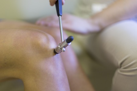 Performing a neurological exam in doctor office. The doctor conducts neurology examination of knee reflex of patient using neurological rubber hammer, checking on presence of disease or pathologyの写真素材