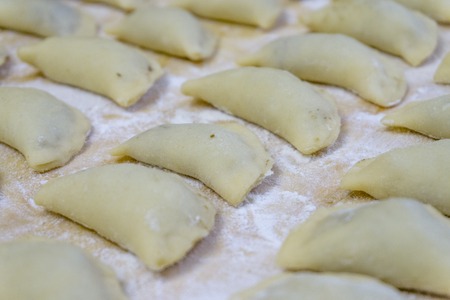 Traditional Russian food dumplings or vareniki, dough with meat or other stuffing, with flour and egg served on a table with sour cream, mushrooms and fresh vegetables, garlic sauce. traditional antique serving in earthenware. Also knows as pelmeni and smetanaの写真素材