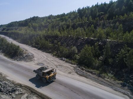 Huge industrial dump truck in a stone quarry loaded transporting marble or granite shot from a drone...