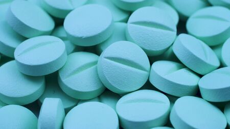 A lot of identical round green dietary supplements lie together closeup rotationの写真素材
