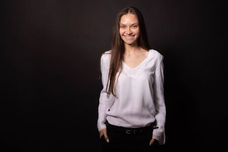 Beautiful girl stands over isolated black background laughing, hands in pocket