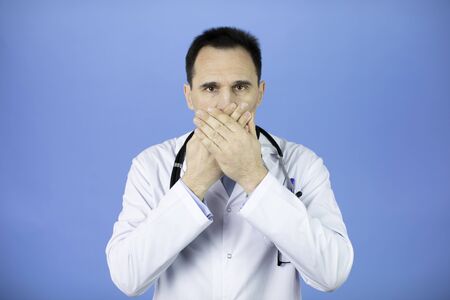 Doctor covers his mouth his palms. Confidential information. Blue background