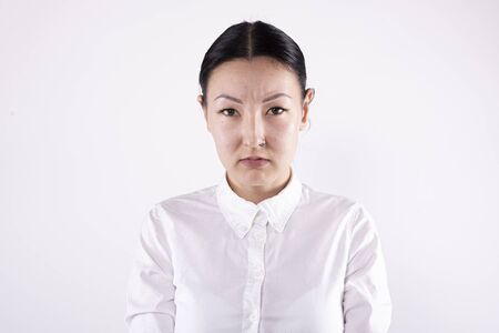 Asian woman with gathered hair in white shirt looks displeased. White backgroundの写真素材