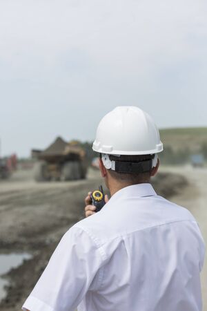 Mining engineer in white shirt and helmet supervises driving dumpers in quarryの写真素材