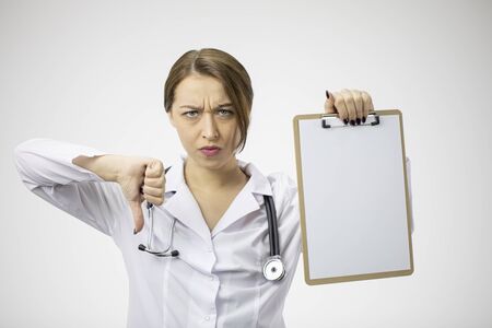 Angry female doctor with blank clipboard showing sign dislike with thumbs downの写真素材