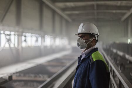 Mining engineer in white helmet and respirator inspects dusty dirty workshopの写真素材