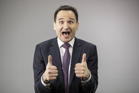 Enthusiastic businessman shows like signs on isolated gray backgroundの写真素材