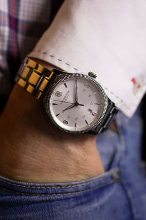 Ibach, Switzerland 31.03.2020 - Closeup fashion image of Victorinox watch on wrist of man: mans hand in blue jeans pocket with white cuff of plaid shirt. Victorinox man watch stainless steel case, white clock face dial stainless steel bracelet swiss quartのeditorial素材
