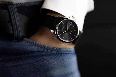 Saint-Imier, Switzerland 31.03.2020 - Closeup fashion image of Longines watch on wrist of man: mans hand in blue jeans pocket with white cuff of plaid shirt. Longines man watch stainless steel case Longines man watch stainless steel case black clock face のeditorial素材