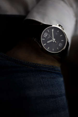 Saint-Imier, Switzerland 31.03.2020 - Closeup fashion image of Longines watch on wrist of man: mans hand in blue jeans pocket with white cuff of plaid shirt. Longines man watch stainless steel case Longines man watch stainless steel case black clock face のeditorial素材