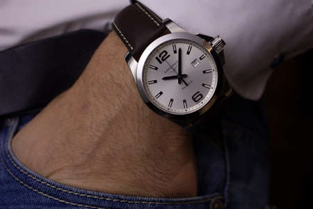 Saint-Imier, Switzerland 31.03.2020 - Closeup fashion image of Longines watch on wrist of man: mans hand in blue jeans pocket with white cuff of plaid shirt. Longines man watch stainless steel case Longines man watch stainless steel case white clock face のeditorial素材