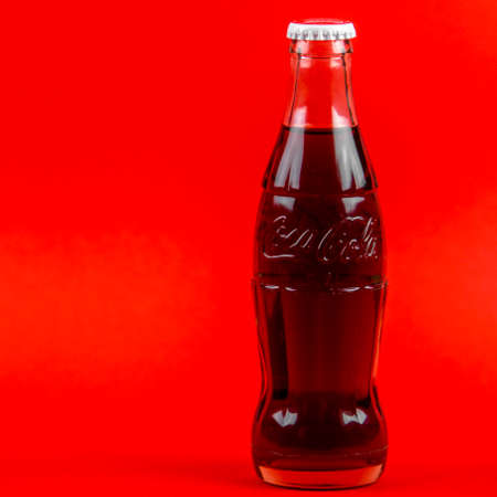 Atlanta, Georgia, USA April 1, 2020: closeup of classic contour glass bottle of Coca Cola embossed logo from USA isolated on red background. concept of globalism, global brand, worldwide spread.のeditorial素材