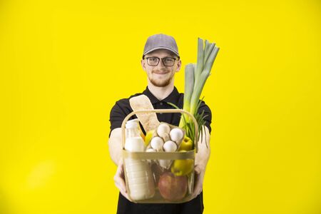 Courier in black uniform holds basket with groceries, focus on delivery manの写真素材