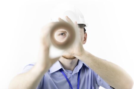 Engineer in safety helmet looks at camera through blueprint twisted into rollの写真素材