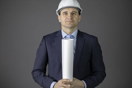 Handsome architect in hard hat holds blueprint roll confidently looks at camera