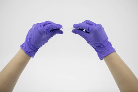 Small glass tube with transparent liquid in doctors hands with rubber glovesの写真素材