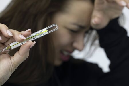 Crying sick girl with headache holds mercury thermometer with high temperature