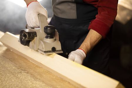 electric planer bevels off wooden workpiece on workbench at cottage workshop. Carpentry work on...