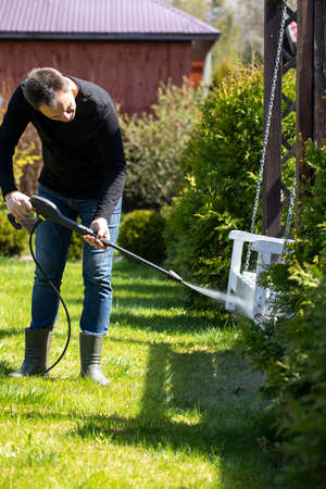 40s man washes wooden swings in country house garden with high pressure washer. Spring cleaning...