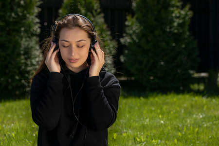Attractive brunette long hair girl dressed in black hoodie listening to music with headphones or...