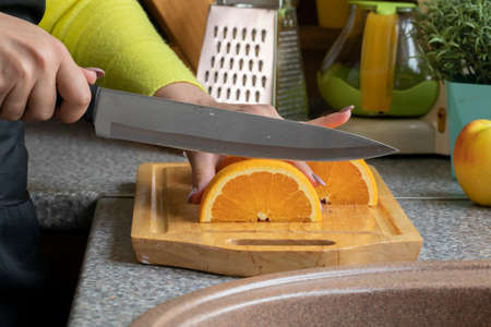 close up of hands young housewife slices oranges with knife in cozy kitchen for lemonade. healthy eating concept.の写真素材