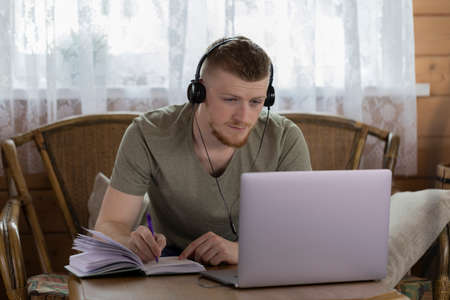 attractive young man in headphones works with laptop, communicates in social networks, gesticulates,...