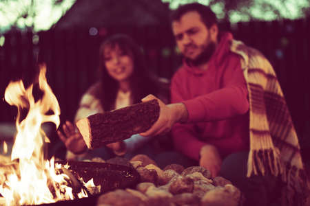 couple of lovers has romantic party by bonfire, young man adds wood to fire. Romantic Weekend. Couple In Love Near Camping In Nature. Inspiration for wedding, date, romantic Vacation Outdoorsの写真素材